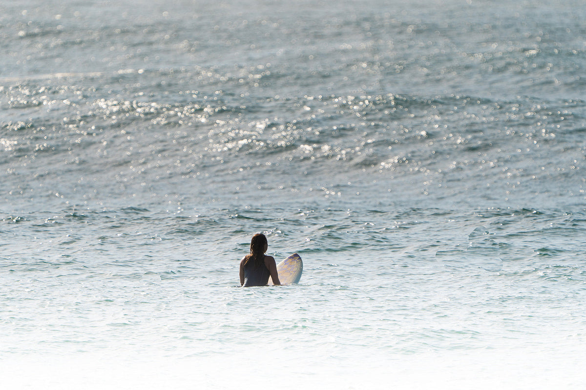 A woman sitting on a surf board waiting for a wave to break